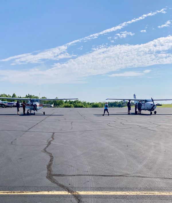 Two small airplanes parked on a runway with people around them under a blue sky.