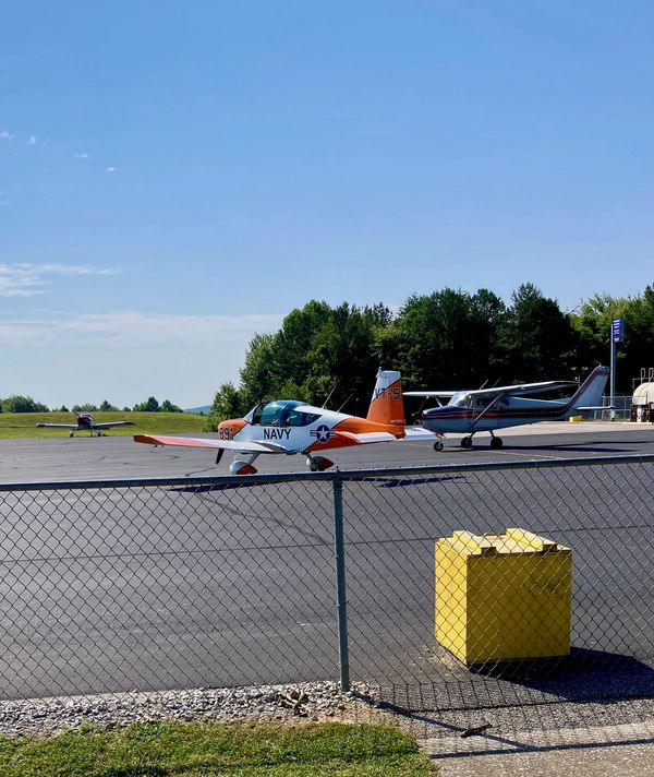 Small Navy training aircraft and private planes on an airfield on a sunny day.