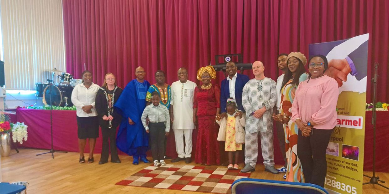 Group photo of diverse people standing indoors with a maroon curtain backdrop.