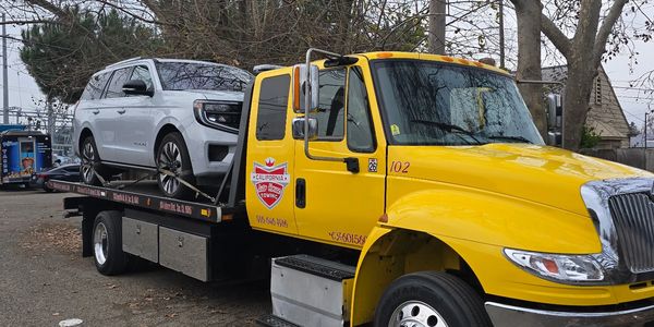 Yellow tow truck carrying a white SUV on a cloudy day.