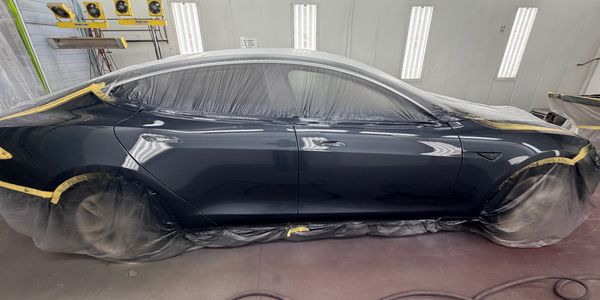 Tesla car masked for painting in a workshop booth.