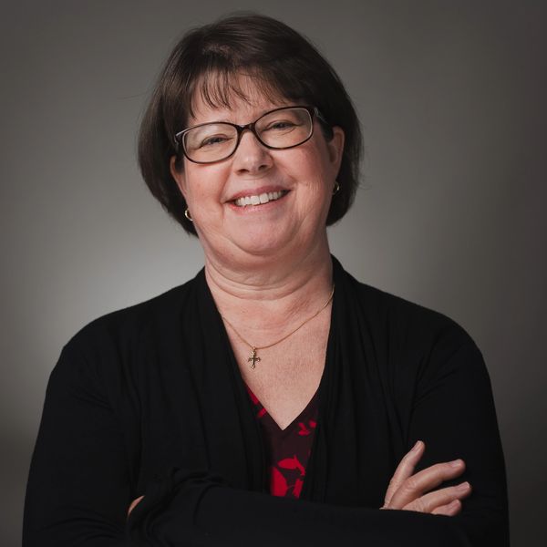 Smiling middle-aged woman with glasses and crossed arms.