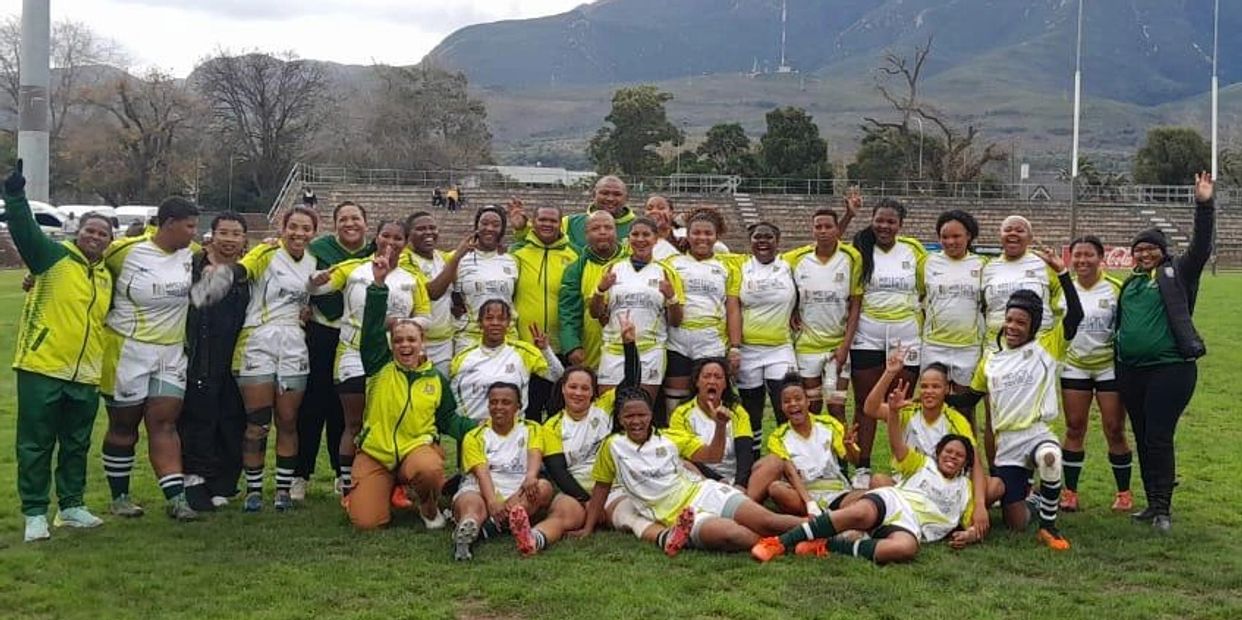 A joyful women's rugby team posing together on the field after a match.