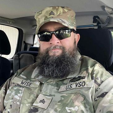 Military personnel in camouflage uniform sitting inside a vehicle.