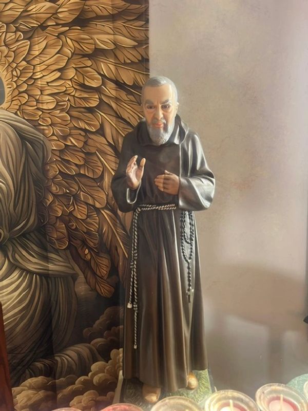 Statue of a bearded monk in a brown robe with prayer beads.