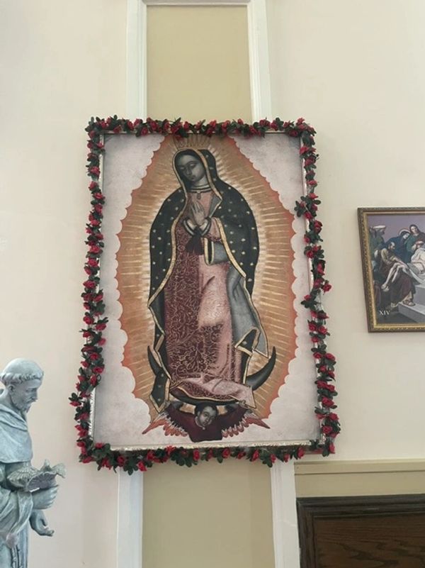 Image of Our Lady of Guadalupe framed with red flowers in a church.