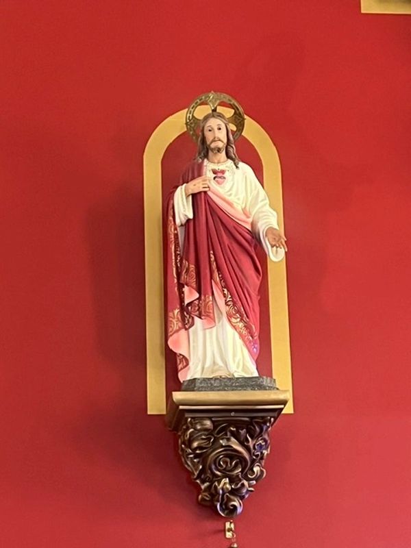 Statue of Jesus with sacred heart on a red and gold wall niche.
