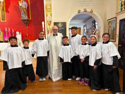 A priest with altar servers in white robes inside a church.