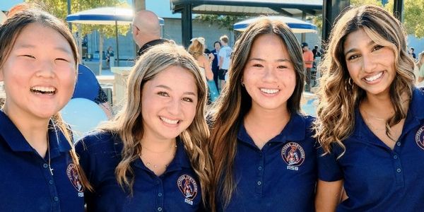 Four smiling young women in navy blue uniforms outdoors.