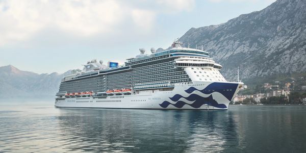 Large cruise ship sailing near mountainous coast under cloudy sky.