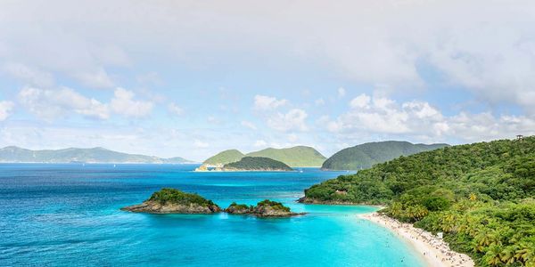 A scenic tropical beach with clear turquoise waters and lush green hills.