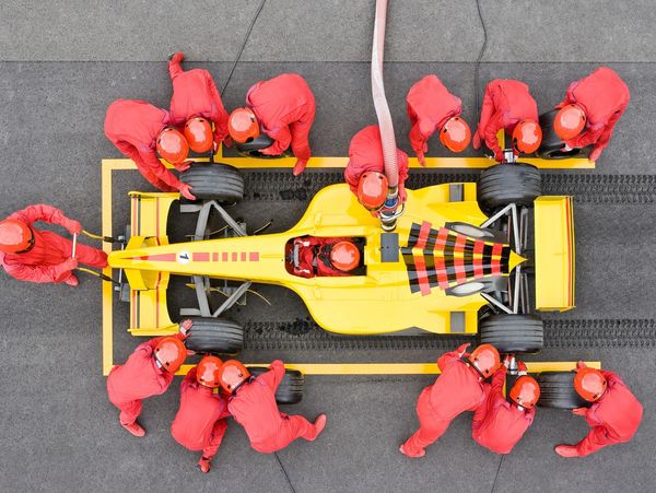 Pit crew in red suits servicing a yellow race car during a pit stop.