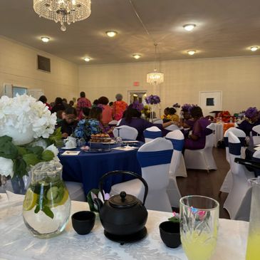 Elegant indoor gathering with white and blue decorations and guests seated at round tables.