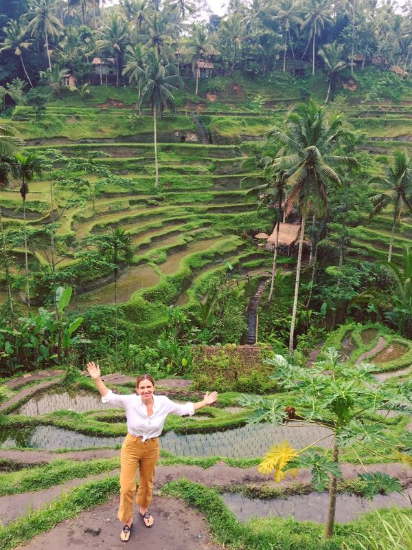 Woman smiling with arms outstretched in front of lush terraced rice fields.
