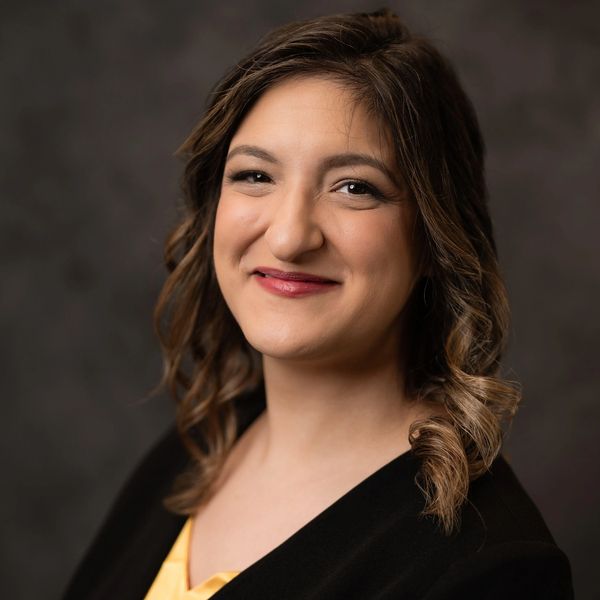 Professional woman with curled hair smiling in a black blazer.