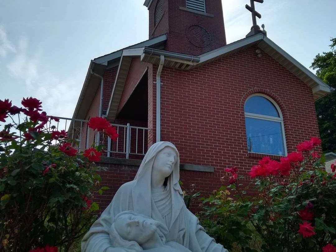 White religious statue in front of a brick church with red flowers.