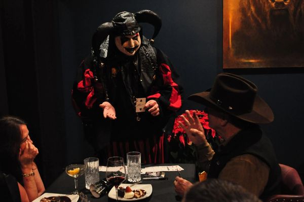 A performer in a jester costume entertains guests at a dinner table.
