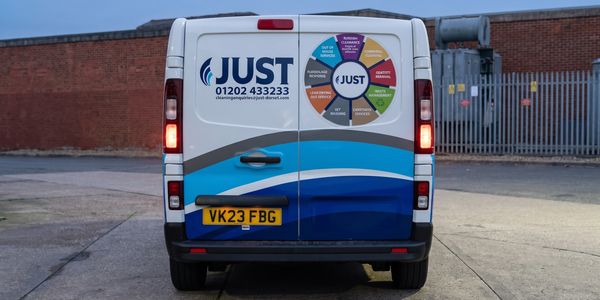 Rear view of a JUST cleaning service van with contact info and services wheel.