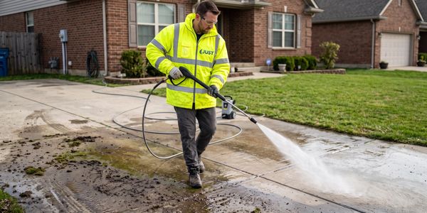 Man power washing a driveway outside a house.