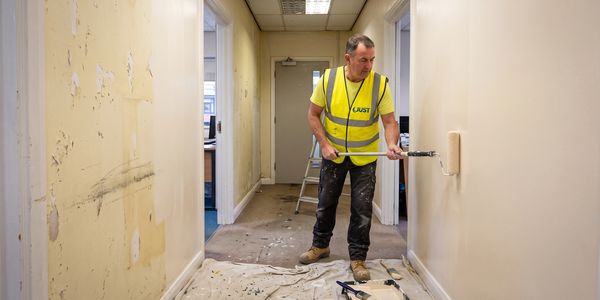 Worker painting a hallway wall with a roller brush.