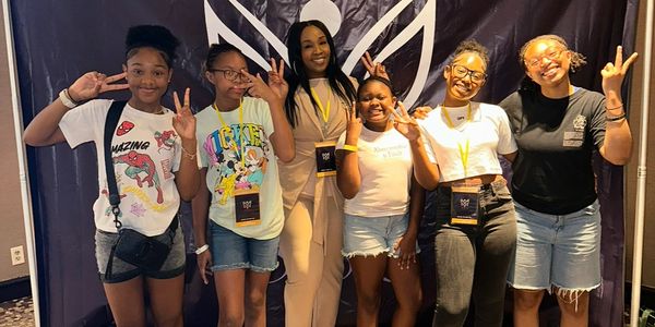 Six smiling girls posing with peace signs in front of a black backdrop.