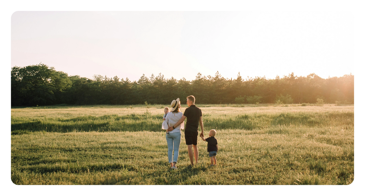 A family of four walking in a sunlit grassy field at sunset.