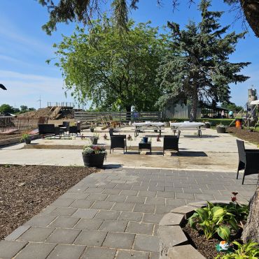 Outdoor seating area with scattered chairs and tables under trees.