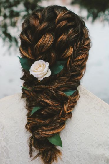 Intricate braided hairstyle with white flower and green leaves.