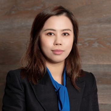 Professional woman in a black blazer and blue blouse against a wooden background.