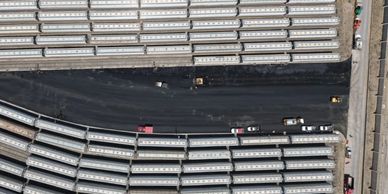 Aerial view of a parking lot filled with white trucks and some vehicles on a paved road.