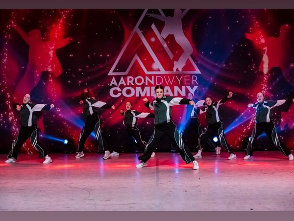 A dance group performing on stage with vibrant red and blue lighting.