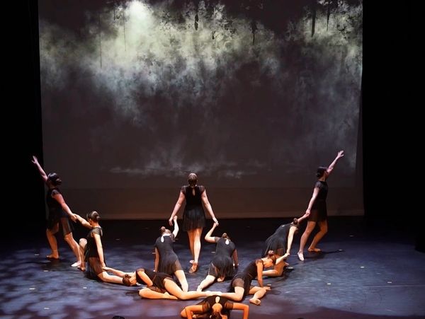 Dancers on stage forming a heart shape in black costumes.