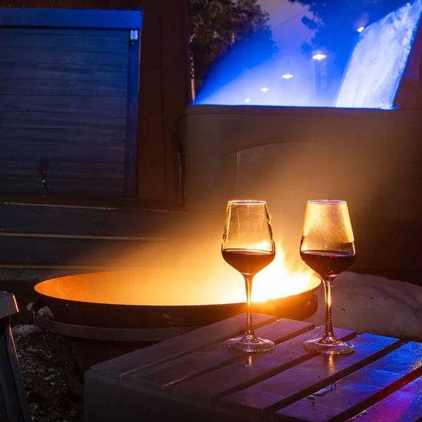 Two glasses of wine on a table by a glowing fire pit at night.