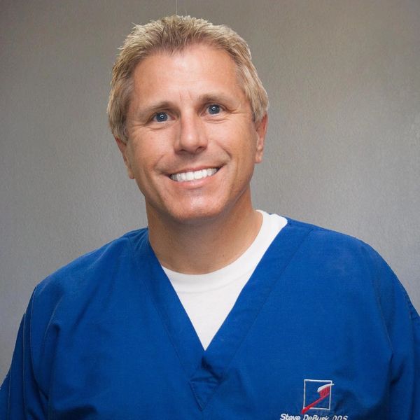 Smiling man in blue medical scrubs against a plain background.