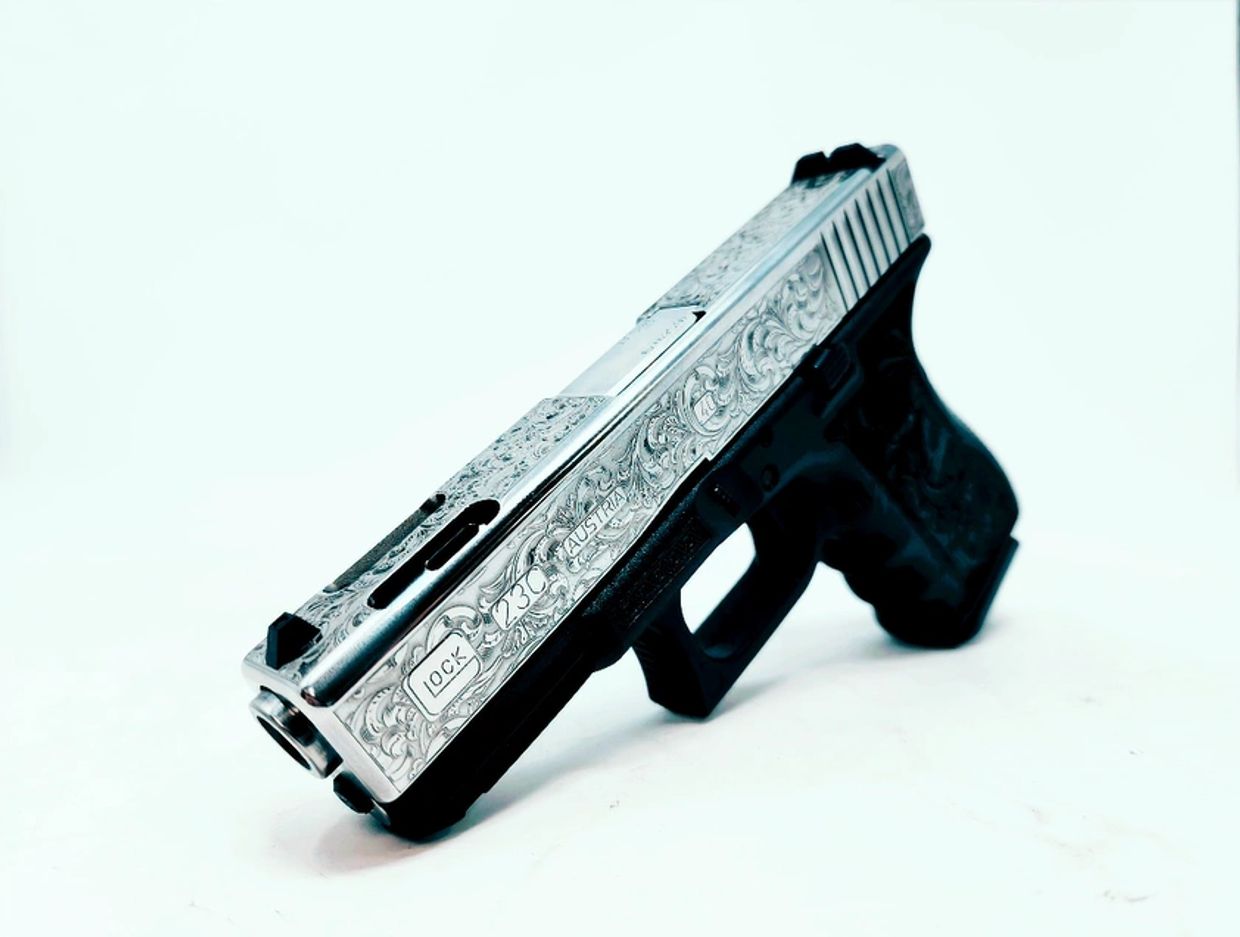 Engraved silver and black Glock 23 pistol displayed on white background.