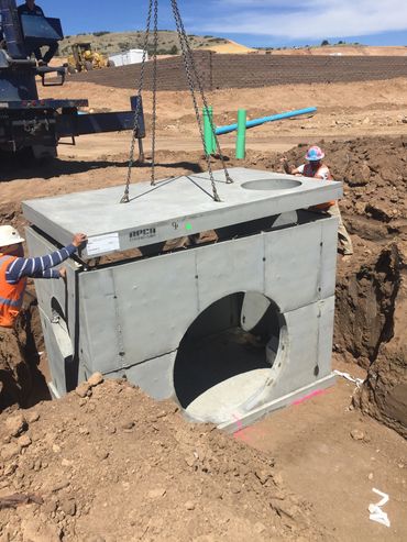 Construction workers install a large concrete structure in an excavation site.