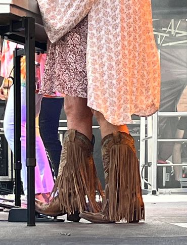 Person wearing brown fringe cowboy boots and a patterned dress.