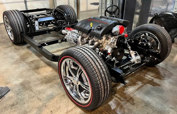 Car chassis with engine and wheels inside a workshop.