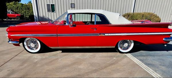 Red vintage convertible car with white roof and whitewall tires.
