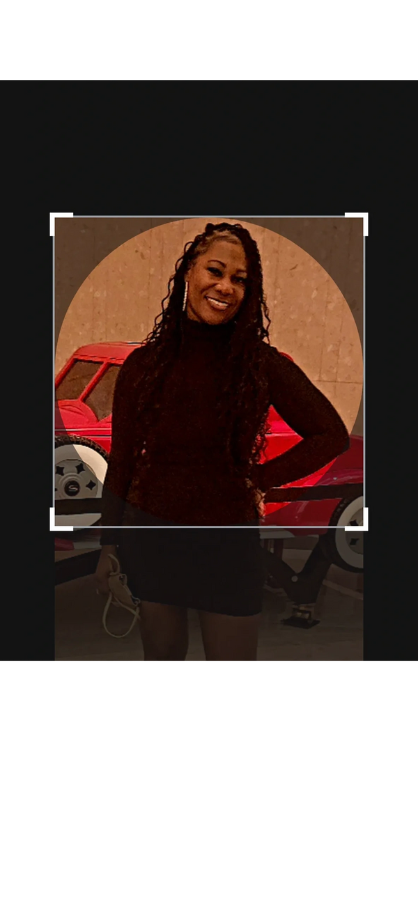 Smiling woman in black dress posing indoors with a red car in the background.