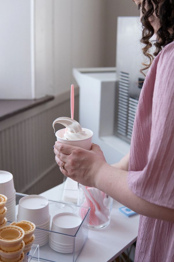 Person holding a cup of soft serve ice cream with a pink spoon.