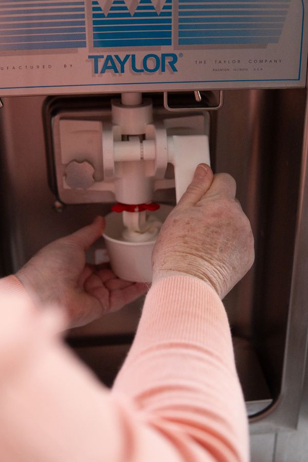 Elderly hands dispensing soft serve ice cream from a Taylor machine into a cup.
