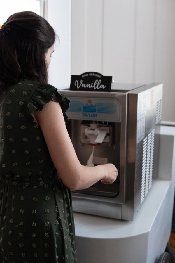Woman serving vanilla soft-serve ice cream from a machine.