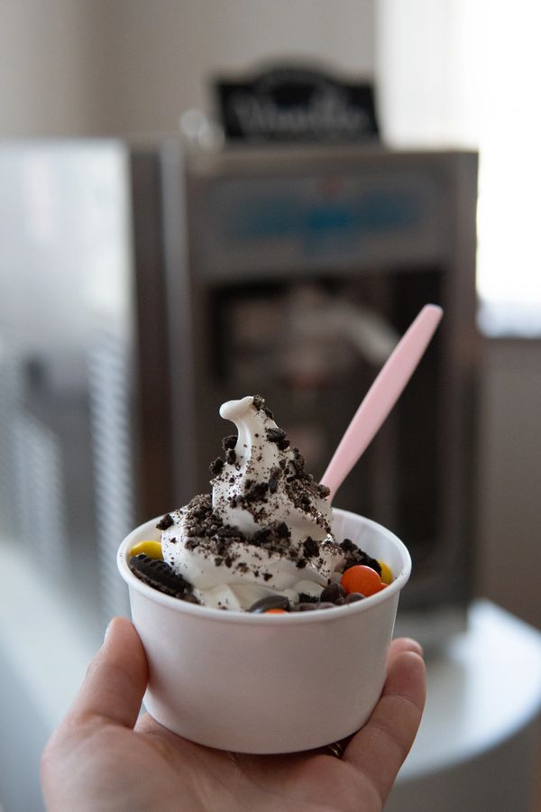Hand holding a cup of soft serve ice cream with cookie crumbs and colorful candy.