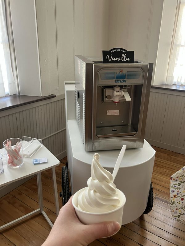 Hand holding vanilla soft serve in a cup near a Taylor soft serve machine.