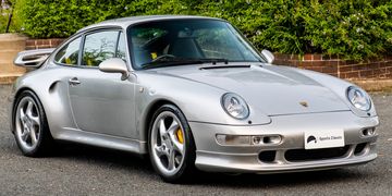 Silver Porsche 911 sports car parked outdoors near greenery.