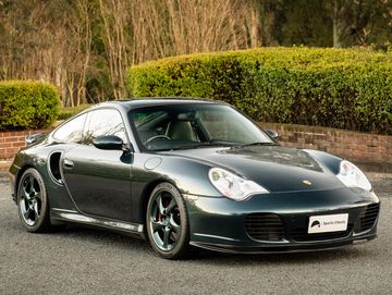 A sleek black Porsche sports car parked outdoors with greenery in the background.