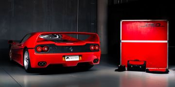 Red Ferrari F355 sports car parked indoors beside a red tool cabinet.
