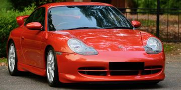 Bright red sports car parked on a street with trees reflected on its hood.