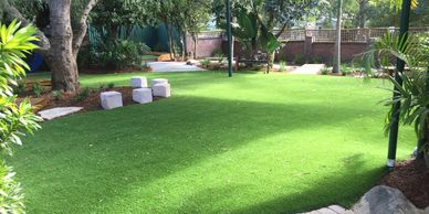 A shaded garden area with artificial grass and stone stools.